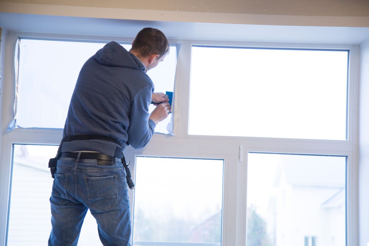 A man painting a window frame with a paintbrush, focused on applying a fresh coat of paint.